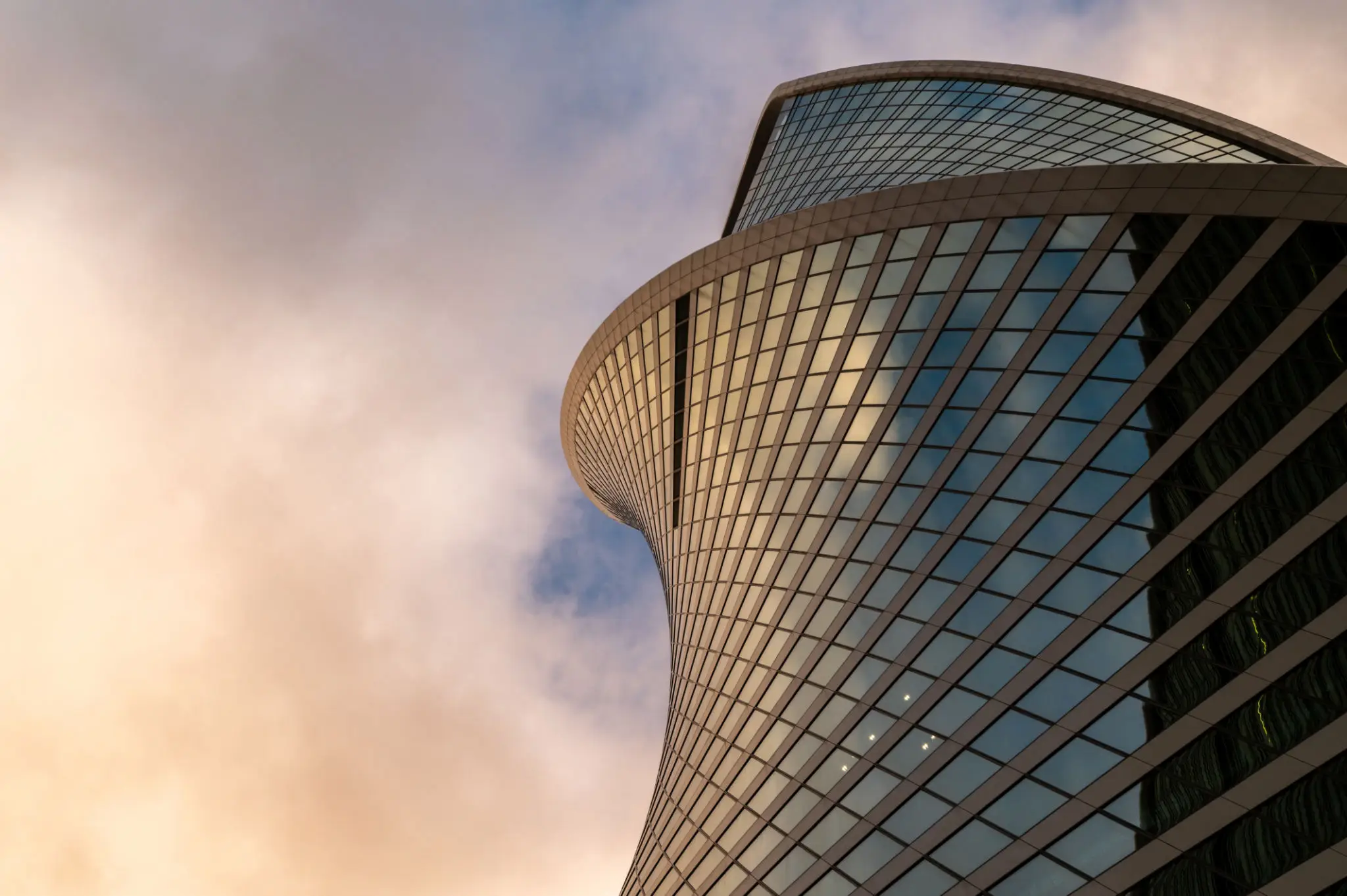 Curved skyscraper against a cloudy sky.